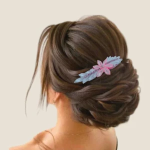 Chignon bas et volumineux de mariée orné d'un accessoire de coiffure fait main avec une fleur en satin rose bonbon centrale et deux feuilles en satin bleu clair, rehaussé d'une rangée centrale de perles roses.