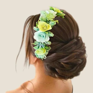Vue de dos d'un élégant chignon bas volumineux pour mariée, orné d'un peigne à fleurs stabilisées vert menthe, jaune et de feuillage botanique au style bohème.