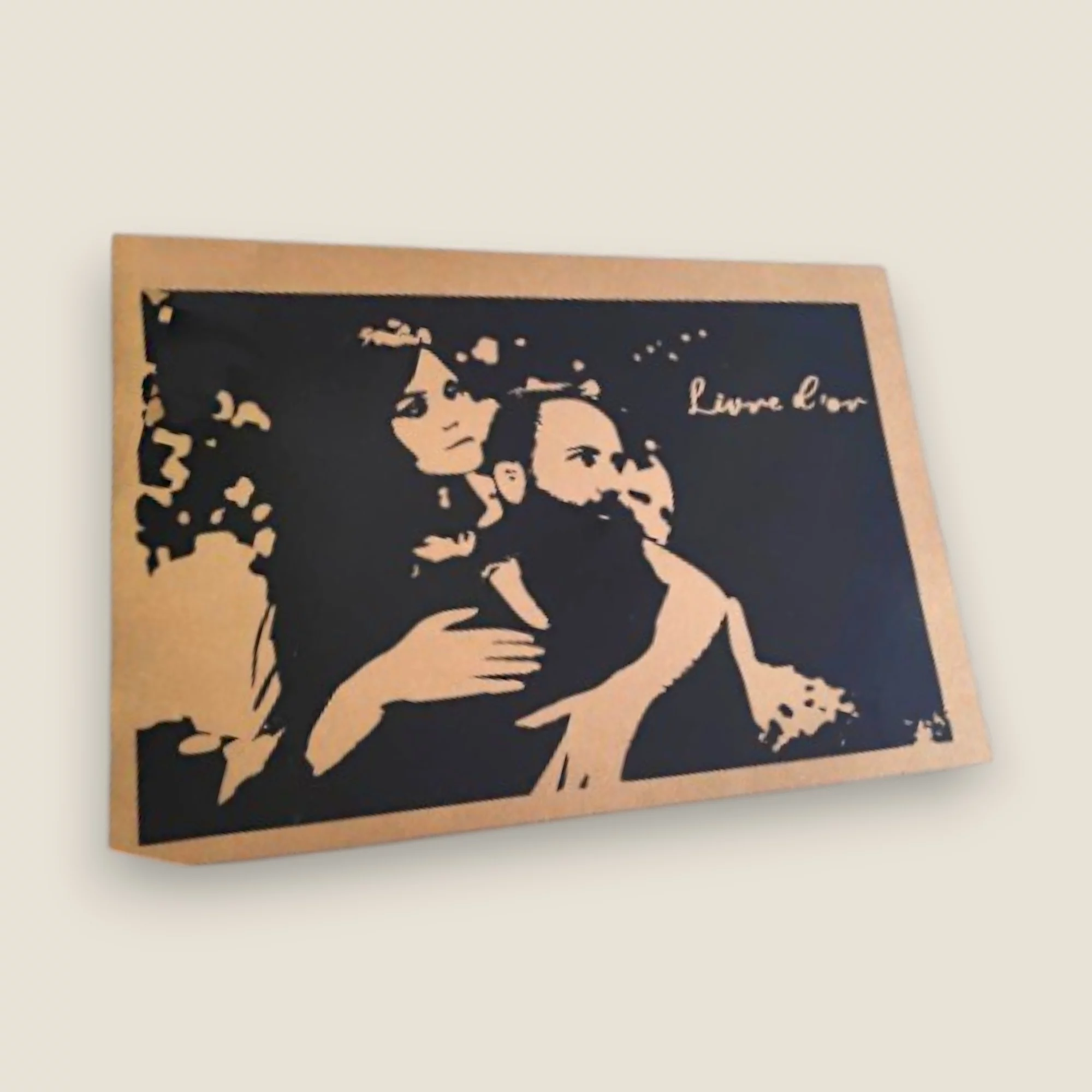 Un livre d'or de mariage rectangulaire au format paysage avec une bordure en carton kraft marron, affichant un grand encadré noir orné de l'illustration stylisée en silhouette des mariés enlacés, avec l'inscription dorée ou kraft "Livre d'or".