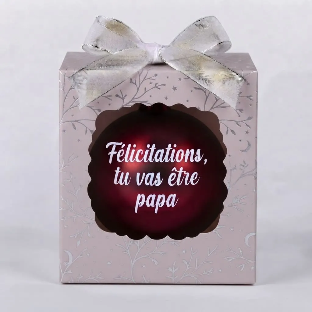 boule-de-noel-felicitations-tu-vas-etre-papa Boîte cadeau rose avec un nœud argenté, contenant une boule de Noël rouge foncé avec le texte "Félicitations, tu vas être papa".