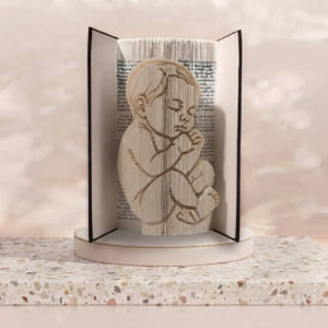 Oeuvre de book folding sculptant le profil d'un bébé endormi en position fœtale, idéal comme cadeau de naissance.