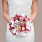 Bouquet de mariée rond fait main avec des fleurs en origami blanches, rouges et en papier livre, orné de plumes, de perles et de tuiles en bois formant le mot OUI.