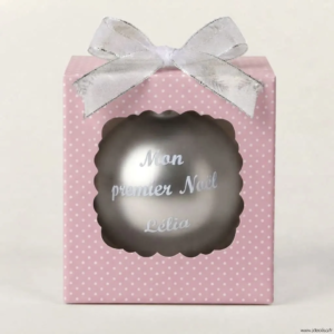 Boîte cadeau rose à pois blancs contenant une boule de Noël personnalisée avec l'inscription Mon premier Noël Lélia