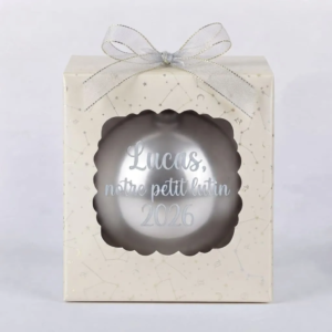 Boîte cadeau beige à motifs d'étoiles et de constellations avec une boule de Noël grise et l'inscription Lucas notre petit lutin 2026
