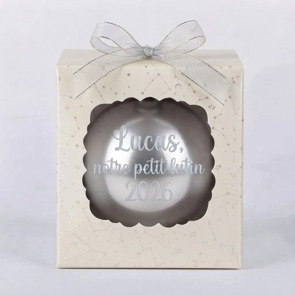 boule de noel personnalisee petit lutin Boîte cadeau beige à motifs d'étoiles et de constellations avec une boule de Noël grise et l'inscription Lucas notre petit lutin 2026