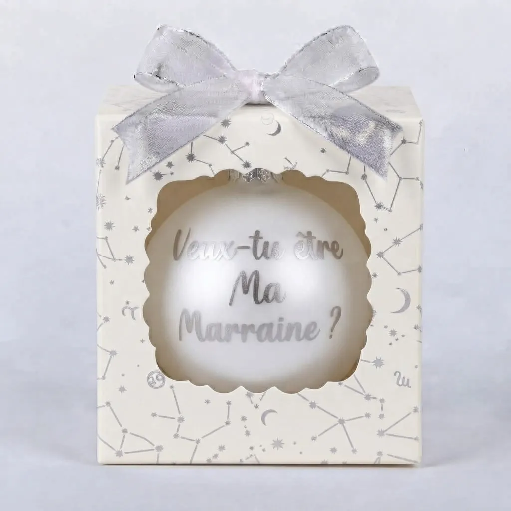 boule-de-noel-veux-tu-etre-ma-marraine bouBoîte cadeau beige à motifs de constellations et d'étoiles avec un nœud argenté, contenant une boule de Noël blanche avec le texte "Veux-tu être Ma Marraine ?".
