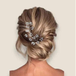 Chignon bas de mariée asymétrique et volumineux orné d'un grand pic à cheveux en perles de nacre argenté