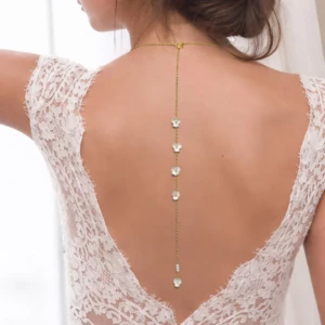 Collier de dos pour mariée en chaîne dorée fine, orné de perles blanches en forme de petites fleurs, porté sur une robe de mariée en dentelle avec un grand décolleté dans le dos.