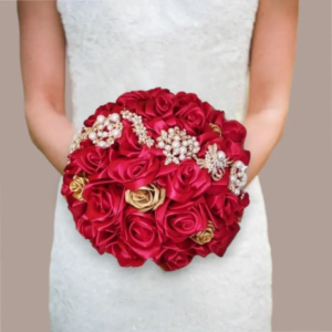 Bouquet de mariée rond fait main avec des roses en ruban de satin rouge et doré, orné de broches dorées et de perles blanches pour un mariage conte de fées.