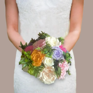 Gros plan sur une mariée tenant un bouquet rond de roses éternelles colorées en papier crépon (orange, violet, rose, blanc) entourées de feuillage vert dense.