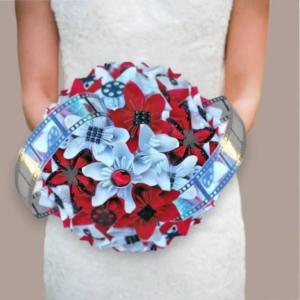 Bouquet de mariée rond fait main avec des fleurs en origami blanches et rouges, entouré d'une véritable pellicule de film de cinéma et orné de détails de cœurs et de perles noires.