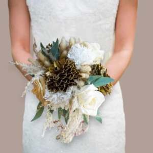 Bouquet de mariée évasé composé d'hortensias blancs, de roses couleur crème, de fleurs séchées texturées et de pommes de pin dorées pailletées, tenu par une mariée en robe de dentelle.