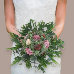 Mariée portant un bouquet évasé composé de roses éternelles en papier rose, crème et terracotta, entourées de feuillages verts et d'eucalyptus.