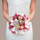 Bouquet de mariée rond fait main avec des fleurs en origami blanches, rouges et en papier livre, orné de plumes, de perles et de tuiles en bois formant le mot OUI.