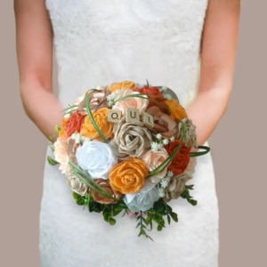 Bouquet de mariée rond et éternel composé de roses en papier crépon orange et terracotta, de roses en satin blanc et beige, décoré de gypsophile artificiel, de brins d'herbe verts et de tuiles en bois formant le mot OUI.