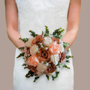 Plan centré sur une mariée portant un bouquet rond composé de roses éternelles artisanales en papier et ruban de satin terracotta, orange pêche et crème, décoré de gypsophile et de brins d'eucalyptus.