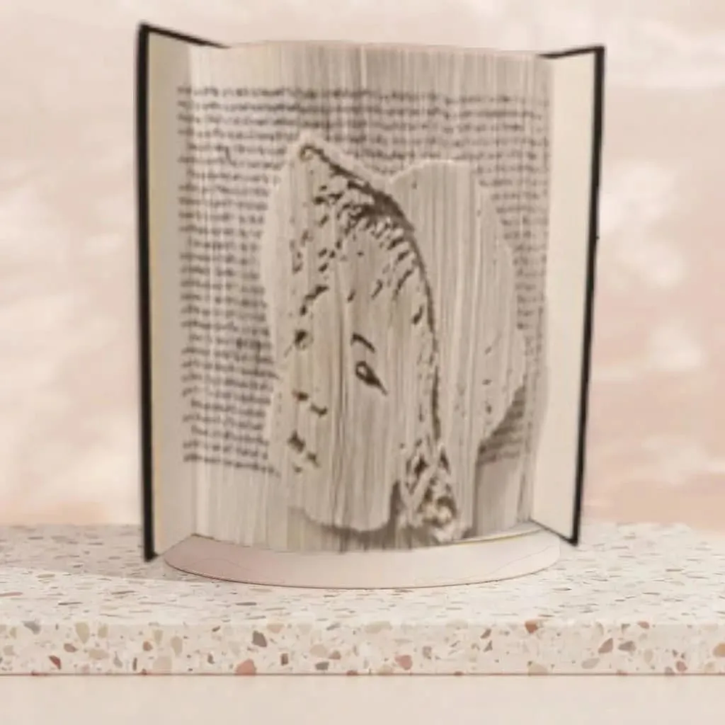 livre-plie-art-portrait-visage-decoration Objet de décoration artisanal en livre plié représentant un portrait de visage vu de profil, posé sur un support en marbre.