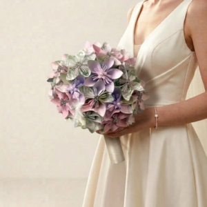 Bouquet de mariée délicat en fleurs origami mauve, rose poudré et vert sauge agrémenté de strass et plumes blanches.