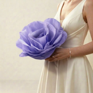 Fleur géante unique en papier crépon violet lilas tenue par une mariée en robe ivoire.